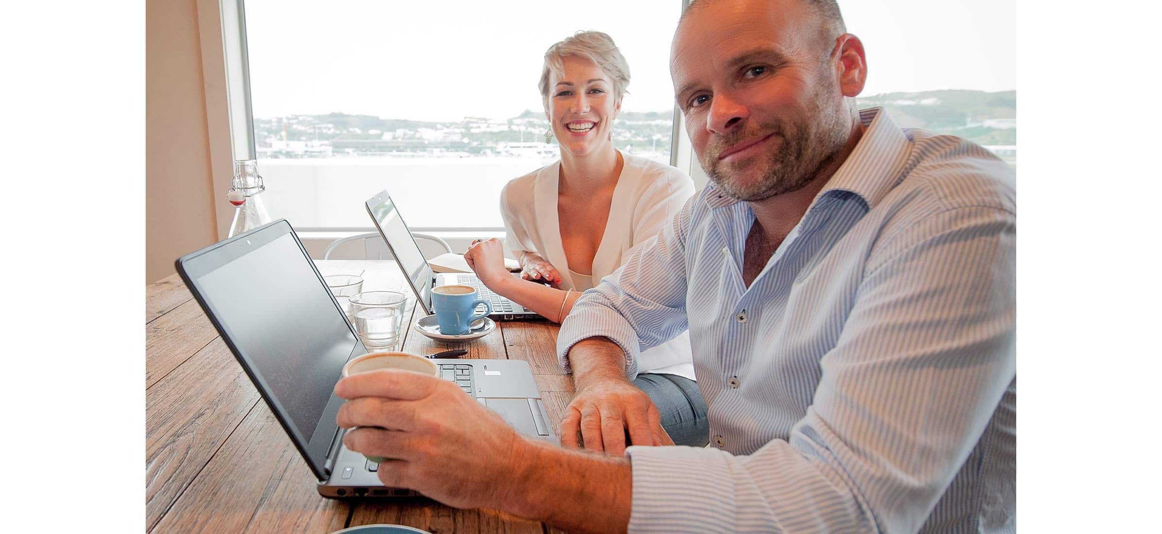 Founders of the Experience Collective, Rosie and Nick Rogers, sitting at a cafe with their laptops open in front of them.